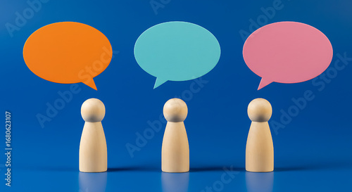 Three wooden figures stand beneath vibrant speech bubbles against a blue backdrop, symbolizing collaborative discussions and communication, ideas