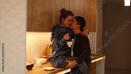 a young couple a playful tea time in their cozy kitchen, filled with love and laughter. They tender interactions as they feed each other, share sweet kisses, and embrace warmly.
