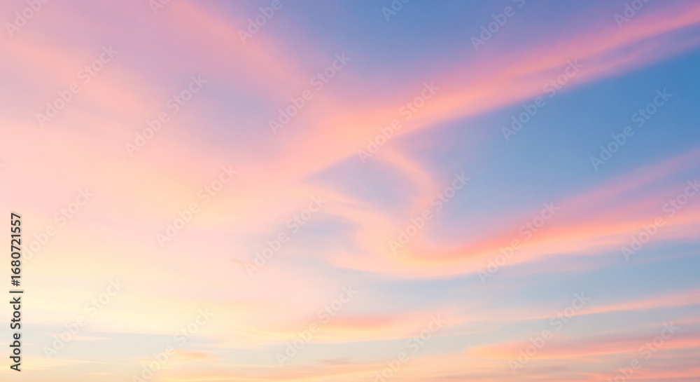 Fototapeta premium Pastel pink and orange clouds drift across a soft blue sky