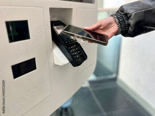 Close-up of teenager paying for takeaway food using mobile phone contactless payment at self-service kiosk. Concept: cashless payments, modern technology, digital everyday life.