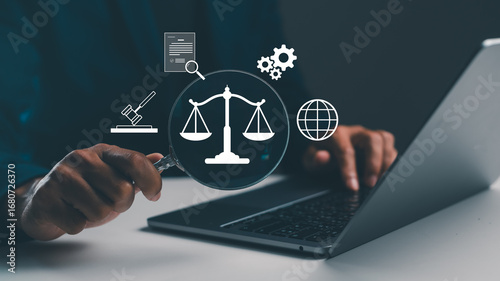 A person holds a magnifying glass over a laptop, inspecting icons related to law, justice, and technology.