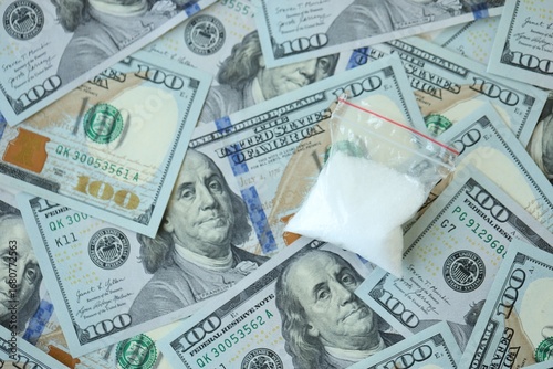 Small cocaine dose in plastic ziplock packet lies on big amount of american currency banknotes