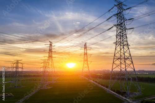 Photos High voltage power tower and transmission lines silhouetted against beautiful su