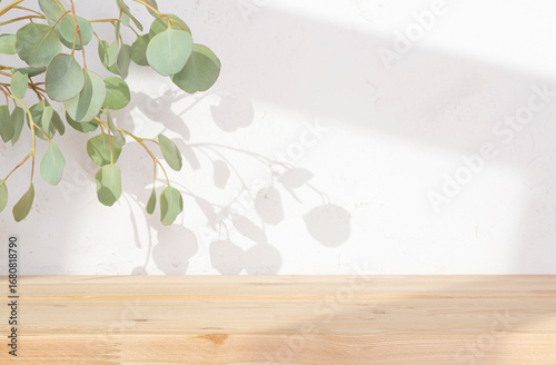 Background for product presentation with wooden table and green eucalyptus leaves branch shadow on plaster wall