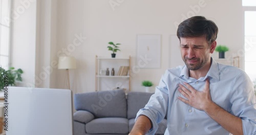 Portrait of young business man sitting alone at the desk with laptop in office suffering from heart attack and chest pain. Male company employee with cardiac health problem. 4k video.