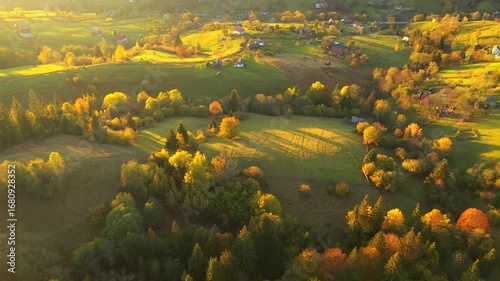A drone flies over a village in a hilly area with autumn trees glowing in the sun. Carpathian mountains, Ukraine, Europe. UHD 4k video.