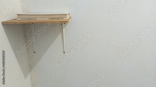 A minimalist wooden wall shelf with white metal supports, mounted on a plain wall with a single book on top. A simple and functional concept for a home or workspace interior.