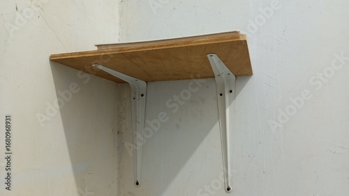 A minimalist wooden wall shelf with white metal supports, mounted on a plain wall with a single book on top. A simple and functional concept for a home or workspace interior.