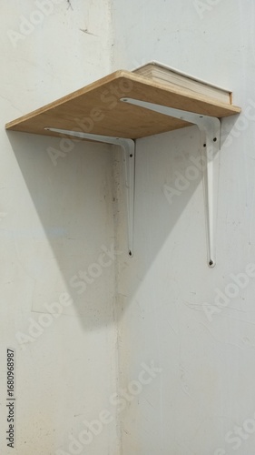 A minimalist wooden wall shelf with white metal supports, mounted on a plain wall with a single book on top. A simple and functional concept for a home or workspace interior.
