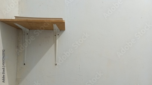 A minimalist wooden wall shelf with white metal supports, mounted on a plain wall with a single book on top. A simple and functional concept for a home or workspace interior.