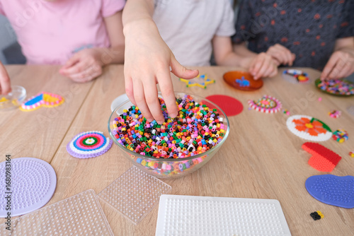 close-up of children's hands creating perler bead patterns, make crafts using thermomosaic technique, beading patterns, perler bead art, concept development of fine motor skills, thermo mosaic ideas