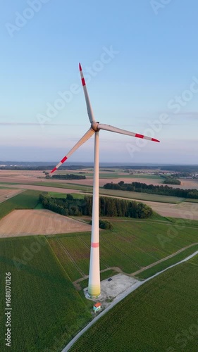 Luftaufnahme einer einzelnen Windturbine im Abendlicht, umgeben von Feldern und kleinen Wäldchen, Symbol für erneuerbare Energie, Hochformat, 4K