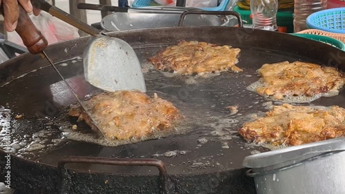 Crispy fried food cooking on large round griddle with hand flipping sizzling street food pancakes in busy outdoor kitchen setting
