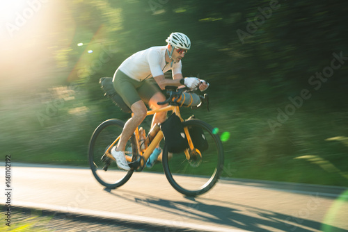 Radfahrer fährt auf gelben Fahrrad und Gepäck auf der Strasse in den Sonnenuntergang, bikpacking, Radreise