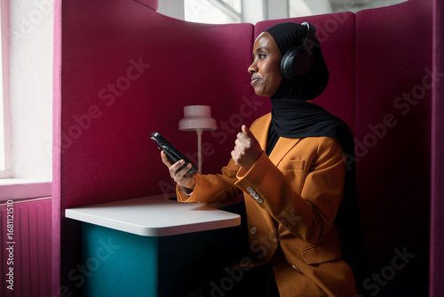 Female entrepreneur wearing wireless headphones while talking on call sitting in modern office space