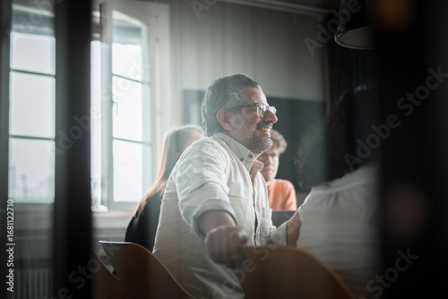 Wallpaper Mural Smiling mature businessman sitting in meeting with coworkers seen through glass at office Torontodigital.ca