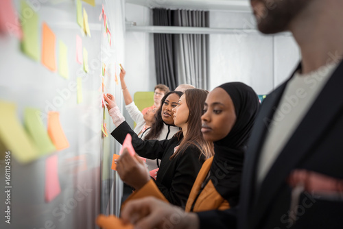 Wallpaper Mural Female business experts discussing ideas while sticking adhesive notes on whiteboard with colleagues in office meeting room Torontodigital.ca
