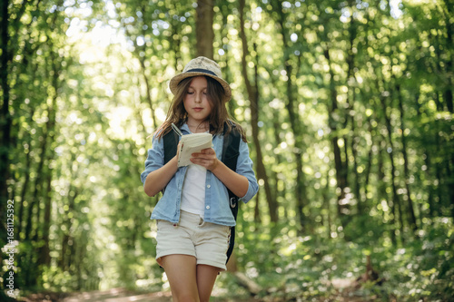 Foto Small notepad is in hands. Young girl hiker is in the forest
