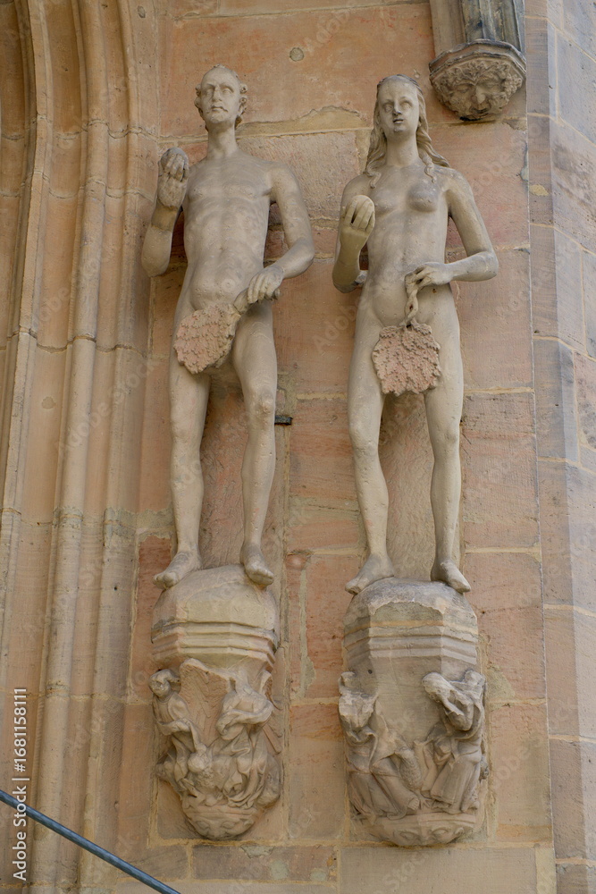 Obraz premium Sandstone sculptures of Adam and Eve at the entrance of the Moritzkirche in Coburg, Germany, showing historic Gothic church figures.