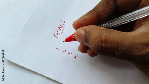 Closeup of hand with red pen underline word goals written on white paper. Ambition, planning, setting goal, aspirations, personal development and motivation concept.