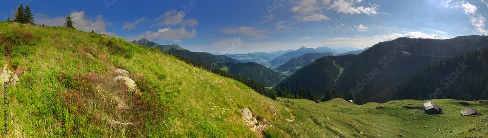 Fototapeta premium Panoramic view of green mountain valley with scattered wooden huts under blue sky