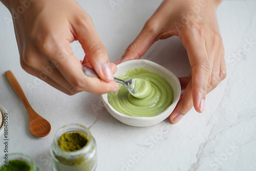 Woman's hands mixing vibrant green matcha paste in a small bowl, minimalist aesthetic, healthy lifestyle concept.