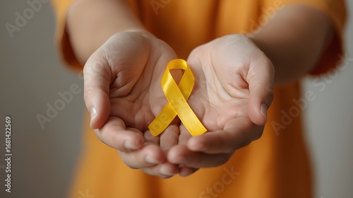 Young female holding yellow gold ribbon awareness symbol for endometriosis, suicide prevention, sarcoma bone cancer, bladder cancer, liver cancer and childhood cancer concept. Health care. Copy space.