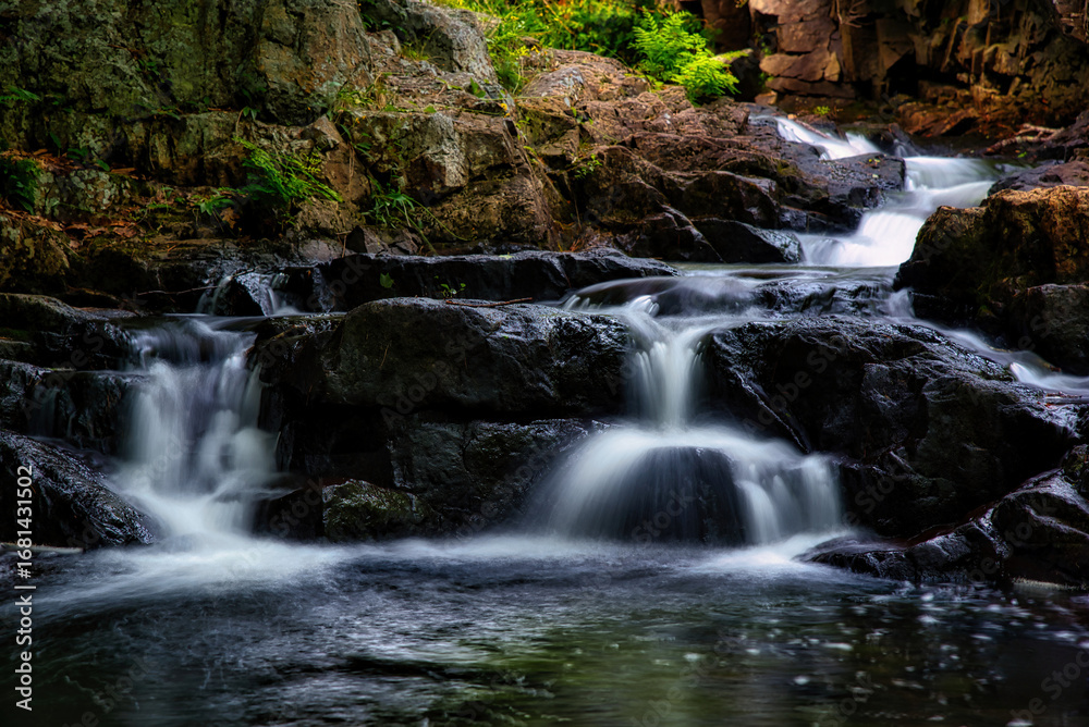 Naklejka premium Silky cascading waterfall flowing over layered rock formations with autumn leaves