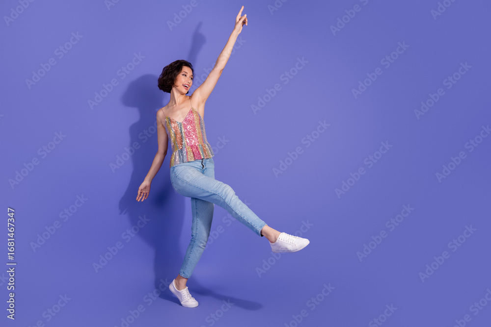 Obraz premium Crazy woman in a shiny sequin top and jeans dancing joyfully against a vibrant purple background