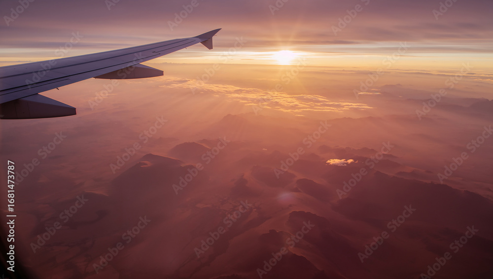 Fototapeta premium Airplane Wing with Sun Setting Behind Mountainous Terrain