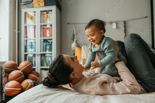 Happy woman playing with baby boy while lying on bed at home