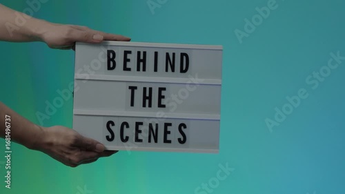 Behind the Scene. Cinematic lightbox sign displaying the text Behind the Scenes held by hands in studio light set. Scene for video film production movie sets backstage moments or creative industry.