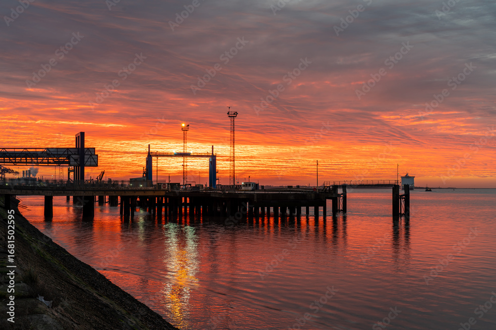 Fototapeta premium Fiery sunrise over the Hull passenger ferry dock with vivid orange skies reflected in calm water,