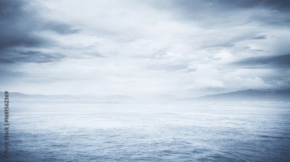 Fototapeta premium A serene coast with calm waters stretches towards the horizon under a sky filled with soft diffused clouds,