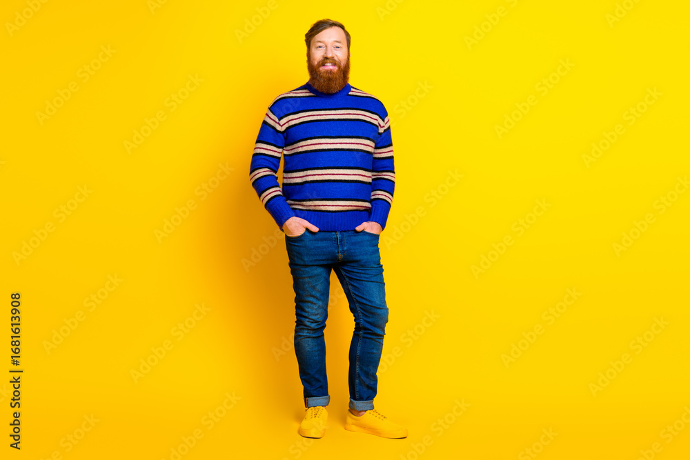 Fototapeta premium Stylish man with a red beard in a striped sweater standing on a yellow background exuding cheerful confidence and casual fashion.