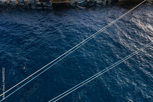 Image of dock lines connecting cruise ship to port rope floating across the surface of ocean water.