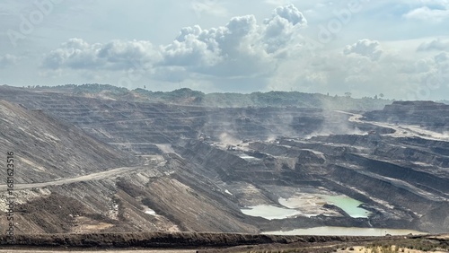 Vast open-pit coal mine landscape with dramatic clouds and industrial scars, showcasing resource extraction's immense scale and impact.