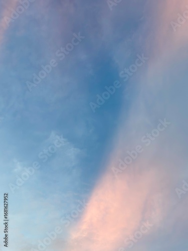 Serene pastel clouds drift across a vast, soft blue sky, creating a peaceful, ethereal atmosphere perfect for tranquil backdrops.