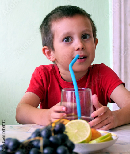 Boy drinking with a straw - Young Boy in a Red T-Shirt Drinking Juice with a Blue Straw