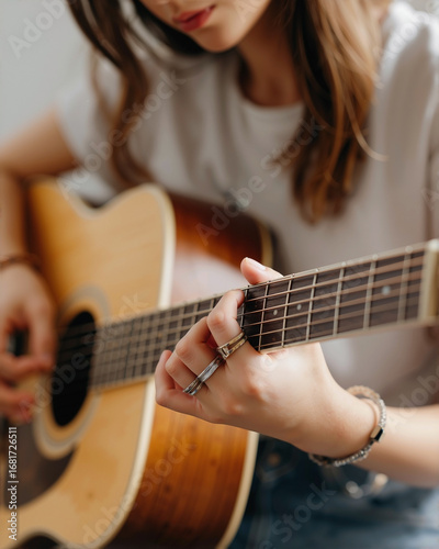 Asian woman's left hand with rings and a metal band, playing chords on an acoustic guitar with her face in soft focus in the background, isolated on white
