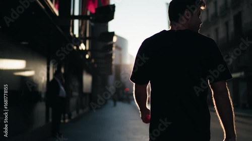 Man walking in urban street at sunrise, sunlight illuminating his silhouette. Represents reflection, vitality, and balance in everyday lifestyle.
