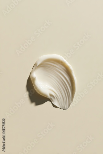 A white cosmetic cream swatch is centered on the right side of an off-white background, with minimal shadows cast by natural light.