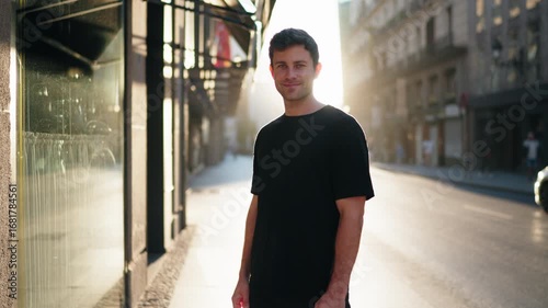 Smiling man standing in sunlit city street, wearing casual black t-shirt. Represents positivity, confidence, and balance in modern urban lifestyle.
