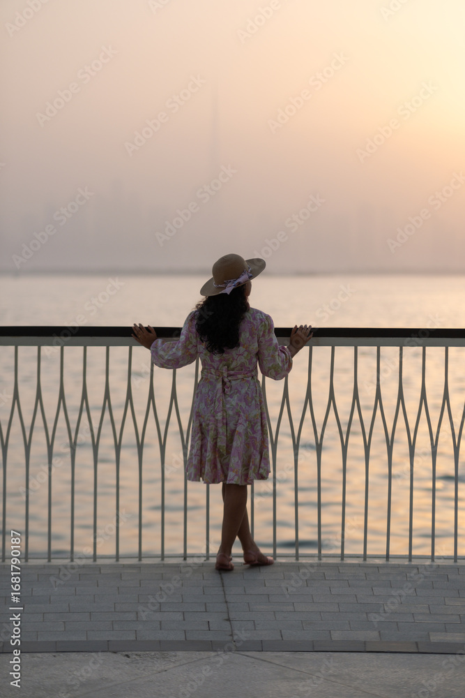 Fototapeta premium Silhouette of girl admiring Dubai city skyline at golden hour, scenic view from Dubai Creek harbor in winter - Vertical stock photo