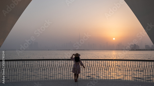 Canvas Print Silhouette of woman watching sunset at Dubai creek harbour with faded Dubai skyl