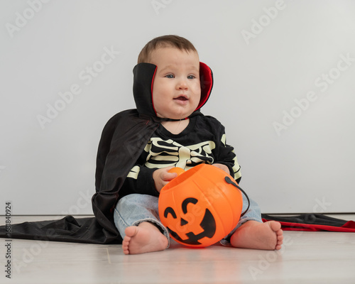 Cute caucasian boy in dracula halloween costume holding candy basket on white background. 