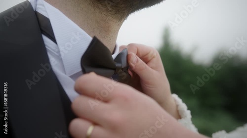 Close-up of a bride’s hands adjusting a groom’s bow tie on wedding day, symbolizing love, care, preparation, and marriage celebration.
