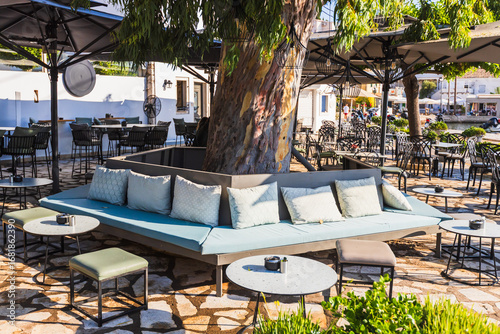 Close-up shot of a chic outdoor cafe lounge area featuring modern, comfortable seating and tables, artistically arranged around a central tree on a sunny day.