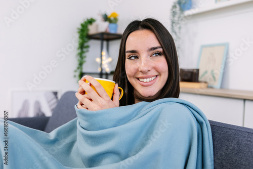 Wallpaper Mural Young pretty woman drinking hot coffee while sitting on sofa at home while looking out the window in winter day. Beautiful girl enjoying hot tea relaxing on couch in the living room Torontodigital.ca