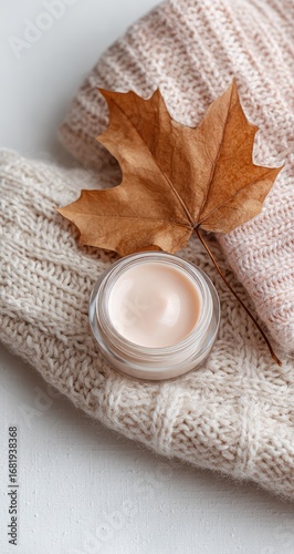 Cream jar atop knitted fabric, autumnal leaf